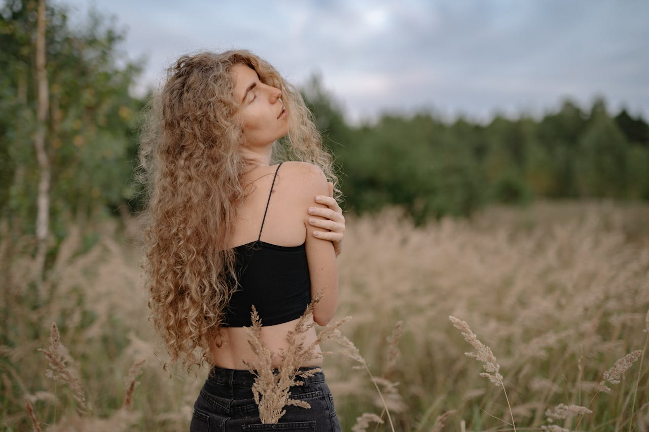 A serene woman with long, curly blonde hair enjoying a quiet moment in a lush field.